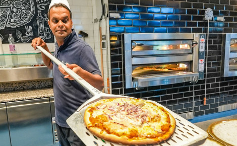 Ein Mann schiebt eine Pizza aus dem Ofen auf einen Teller