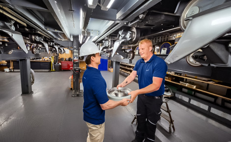 Ein Mitarbeiter des Europa-Park reicht einem anderen Mitarbeiter eine Metallfelge. Die beiden Männer stehen in einer Lagerhalle.