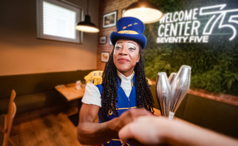Eine Zirkusartistin steht im Café 75 – Welcome Center 75 des Europa-Park. Sie hat drei Jonglierkeulen in der Hand.
