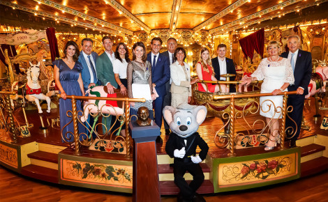 Die Familie Mack steht in einem Karussell des Europa-Park. Im Vordergrund sitzt Maskottchen Ed Euromaus.