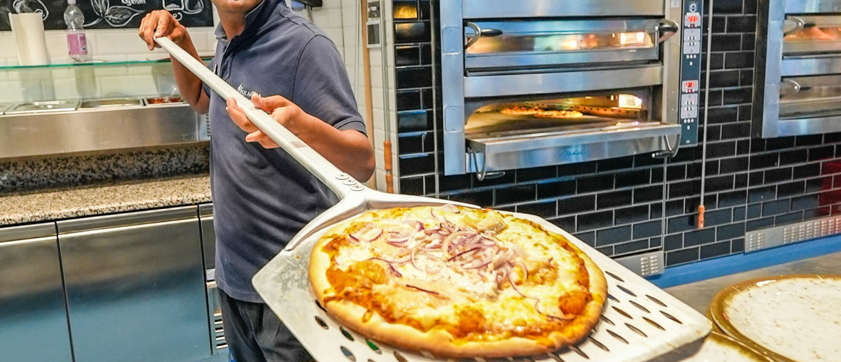Gastronomie in Rulantica Ein Mann schiebt eine Pizza aus dem Ofen auf einen Teller